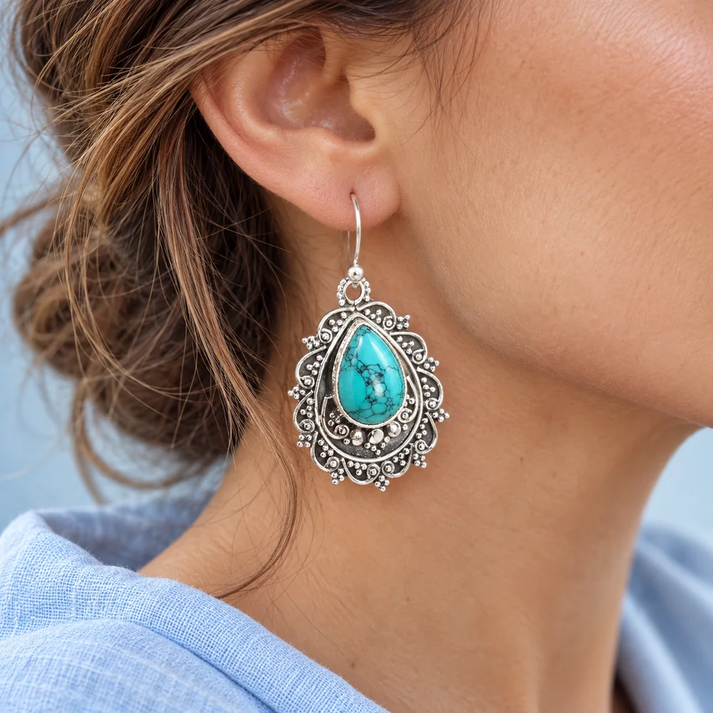 Turquoise druppelvormige oorbel met zilveren details gedragen aan een oor